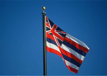 Hawaiian flag waving against clear blue sky.
